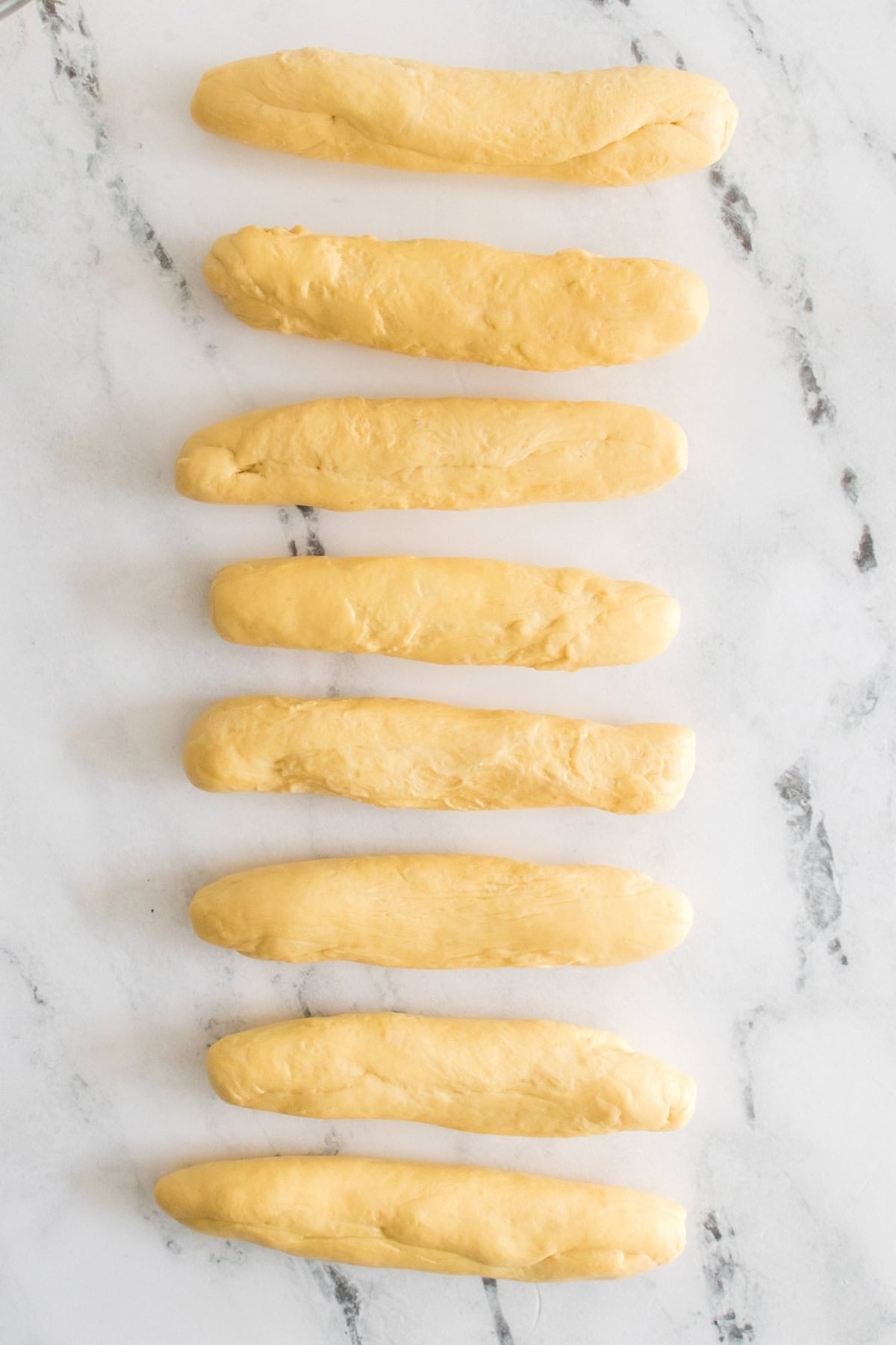 Eight dough pieces lined up on a marble surface.