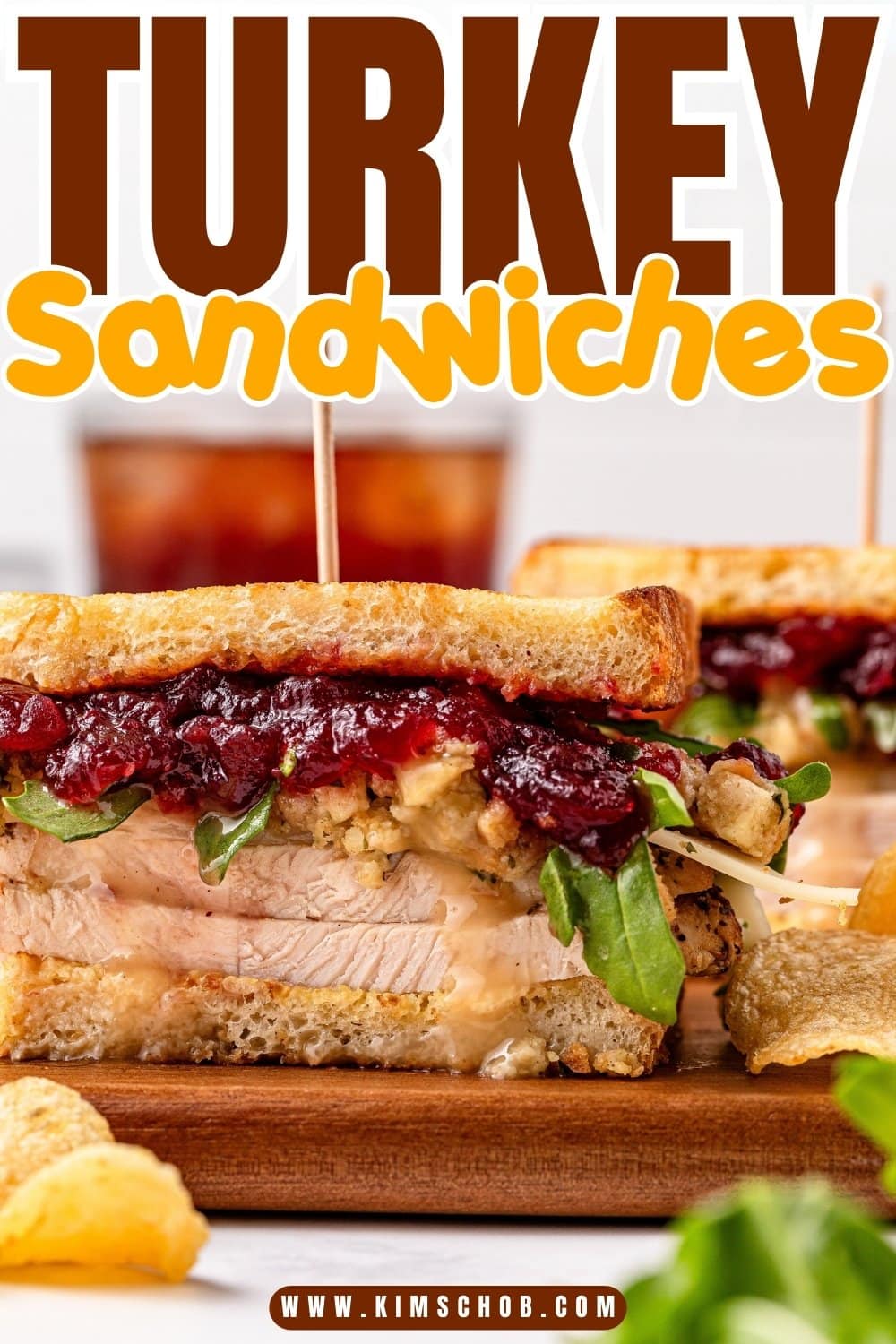 Turkey sandwich with cranberry sauce and greens on a cutting board.
