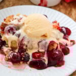 Cherry dump cake topped with vanilla ice cream on a white plate.