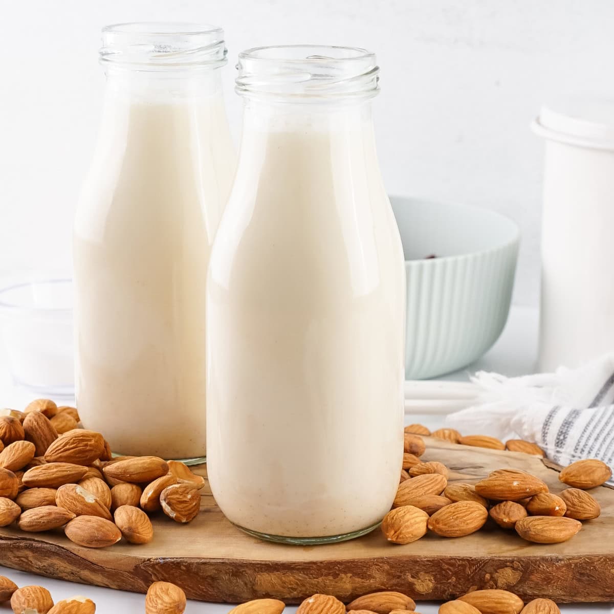 Two glass bottles of almond milk surrounded by scattered almonds.