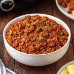 A bowl of seasoned ground beef garnished with chopped herbs.