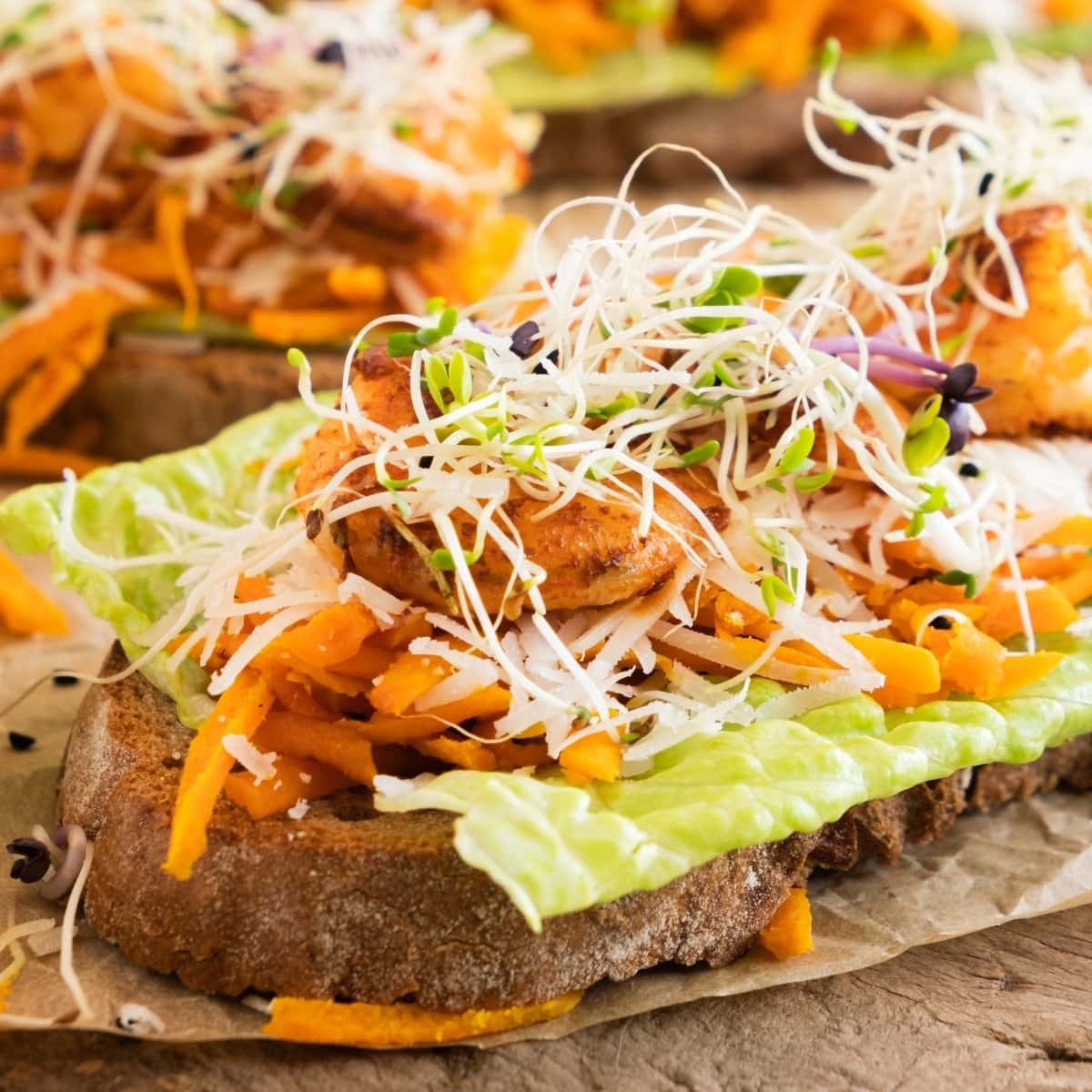 Open-faced sandwich with lettuce, shredded carrot, sprouts, and shrimp.