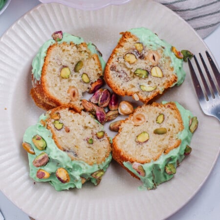 Sliced pistachio cake with green frosting and whole pistachios on a plate.