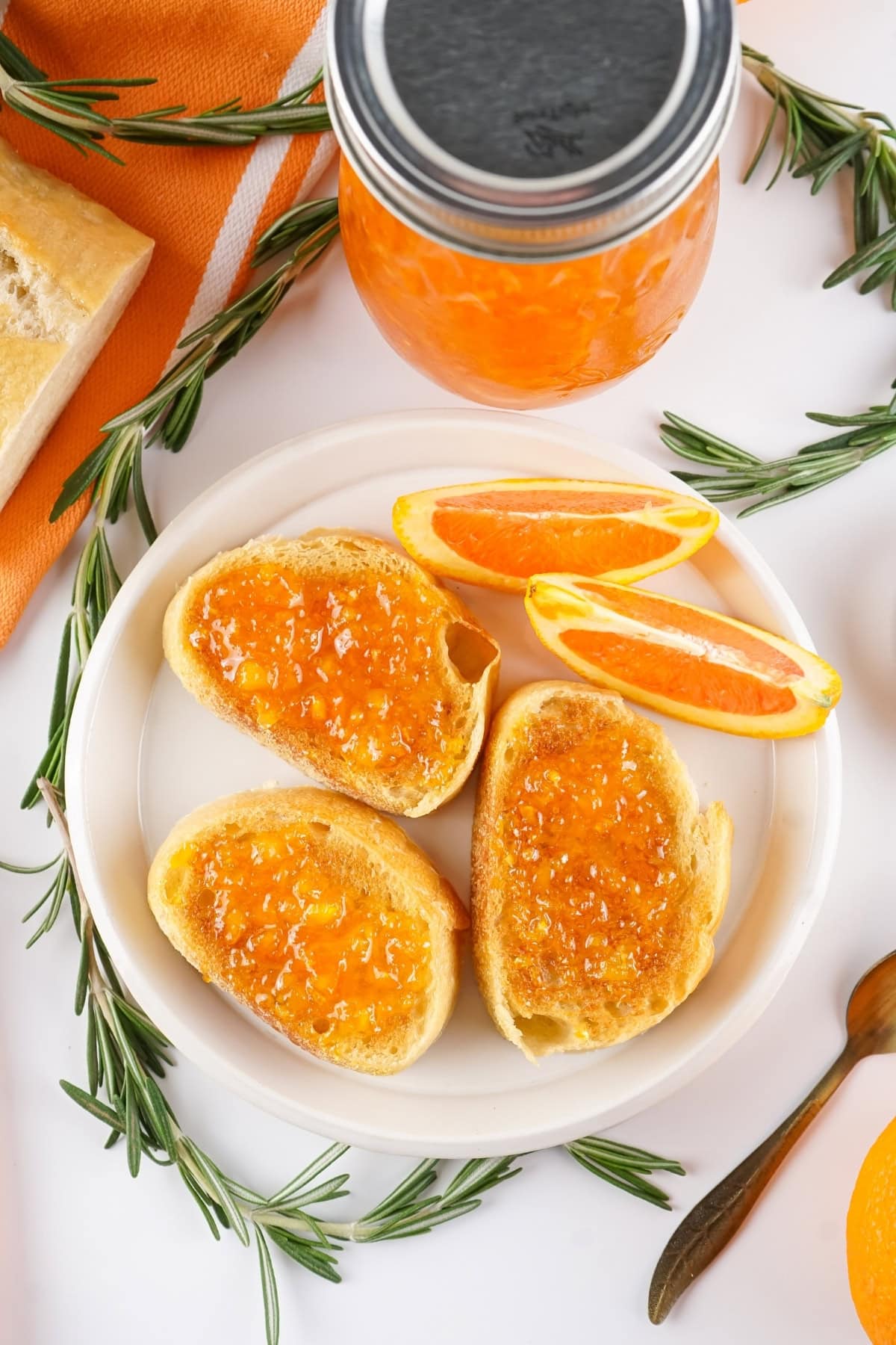 Toast with orange marmalade, garnished with orange slices and rosemary.