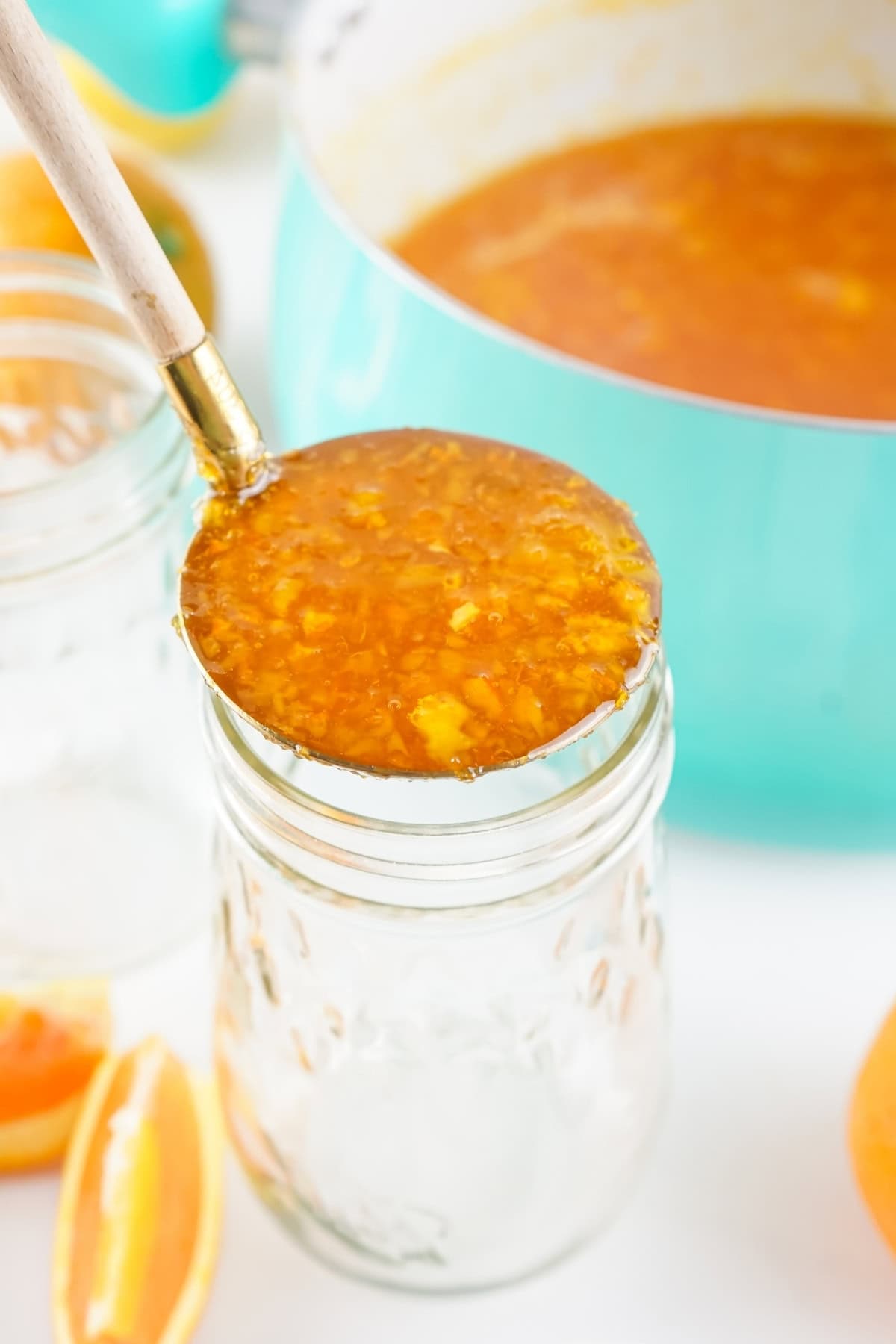 Ladle pouring orange marmalade into a glass jar.