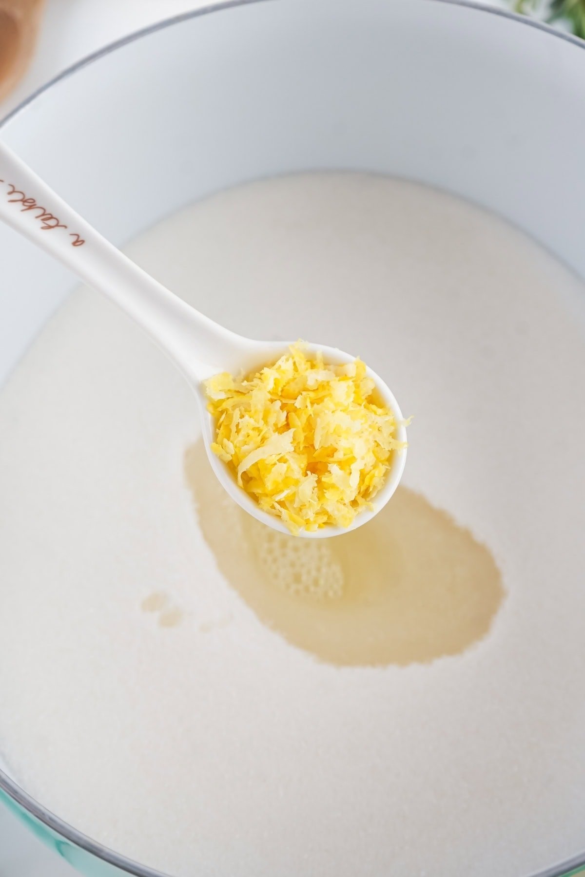 Spoon holding lemon zest over a pot.