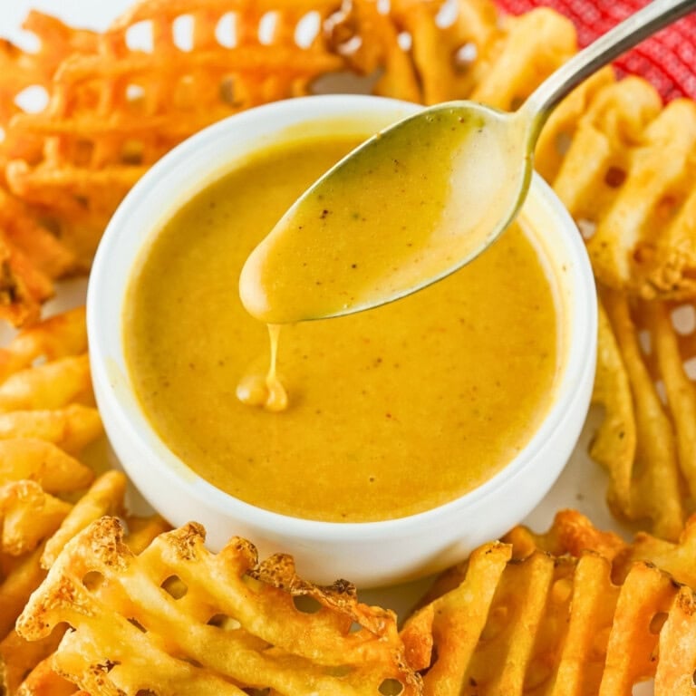 Waffle fries around a bowl of copycat Chick-fil-A sauce with a spoon.