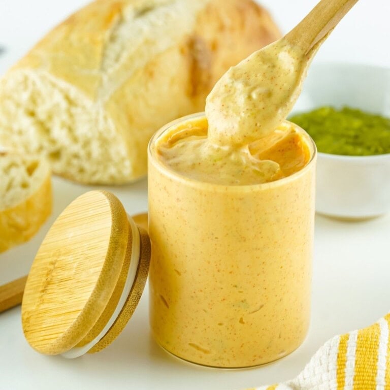 Wooden spoon with sauce from a jar, bread and green dip in the background.