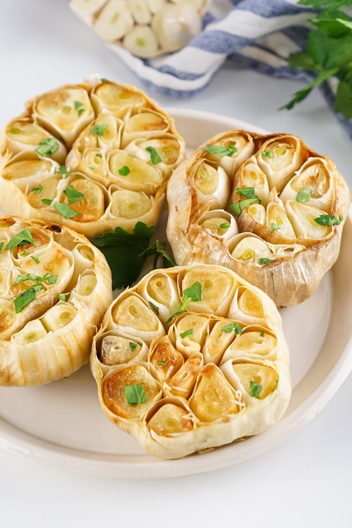 Four roasted garlic bulbs garnished with herbs on a white plate.