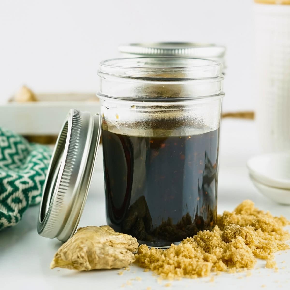 Jar of teriyaki sauce with ginger and brown sugar on a white surface.