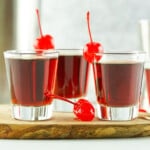 Three glasses of redheaded slut with cherries on top and a wooden board.