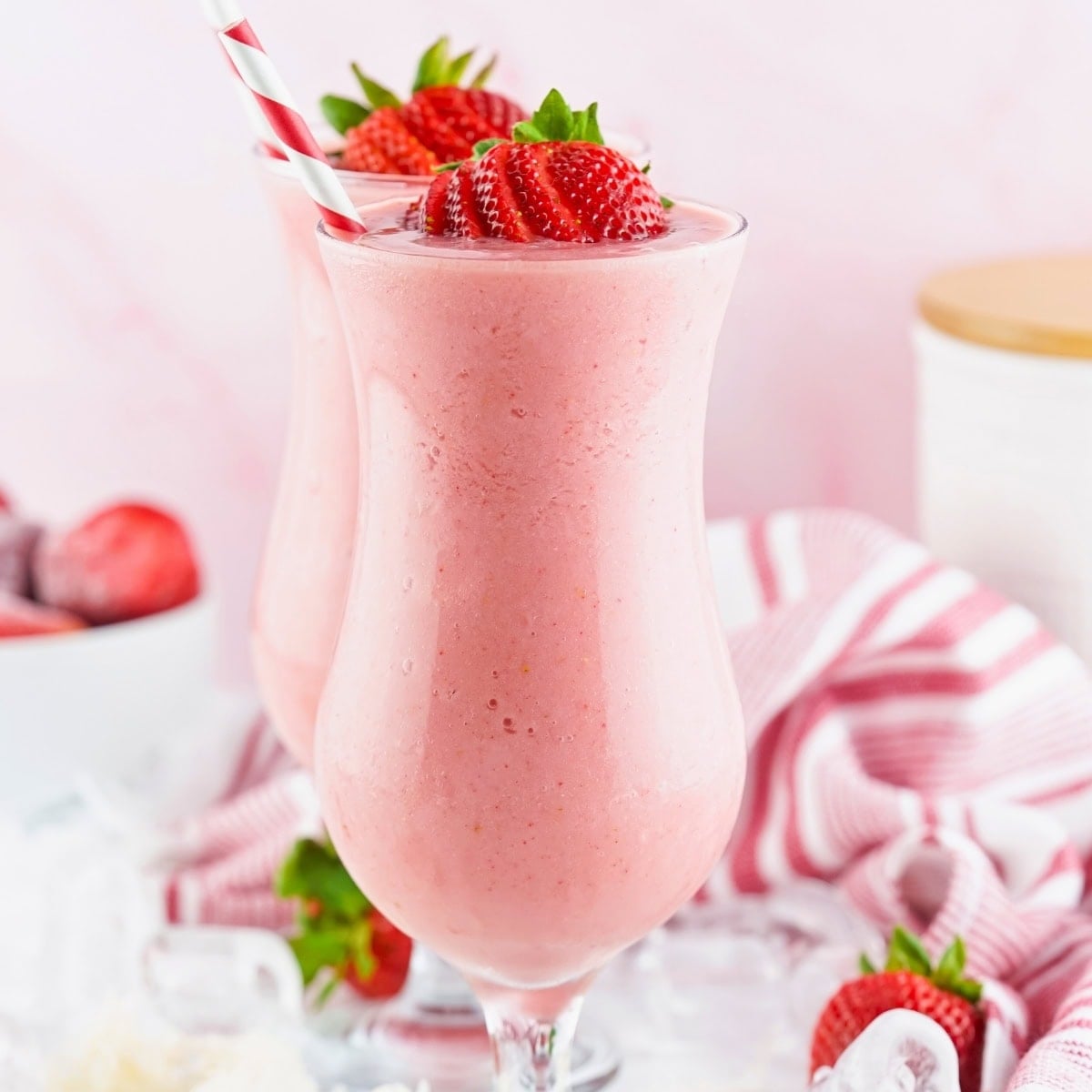 Two strawberry smoothies in tall glasses with striped straws and fresh strawberries.
