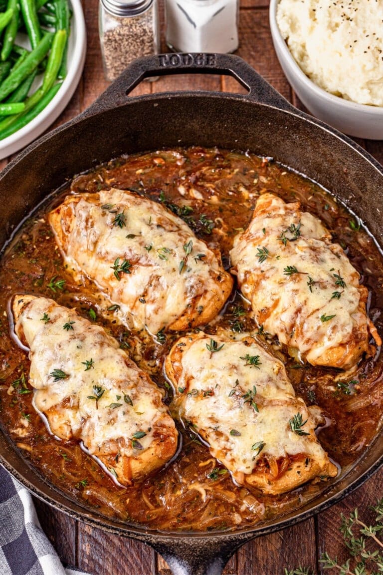 Chicken breasts with melted cheese in a skillet, garnished with herbs.