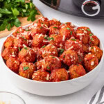 Bowl of meatballs with tomato sauce and grated cheese, garnished with parsley.