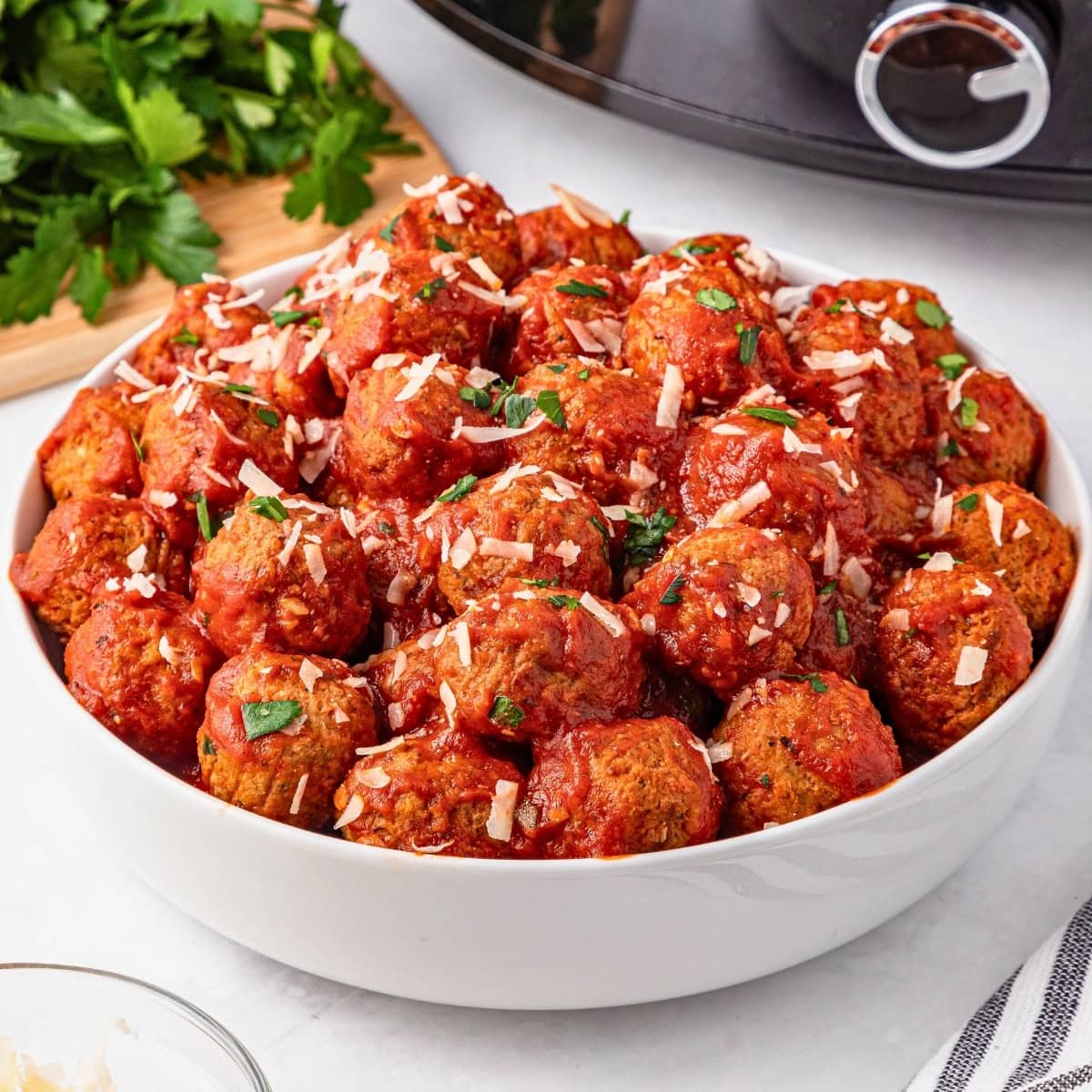 Bowl of meatballs with tomato sauce and grated cheese, garnished with parsley.