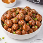 Bowl of glazed meatballs topped with sesame seeds and green onions.