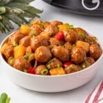 Bowl of meatballs with pineapple, peppers, and green onions on a table.