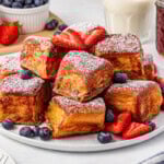 Cubed French toast with berries and powdered sugar on a plate.