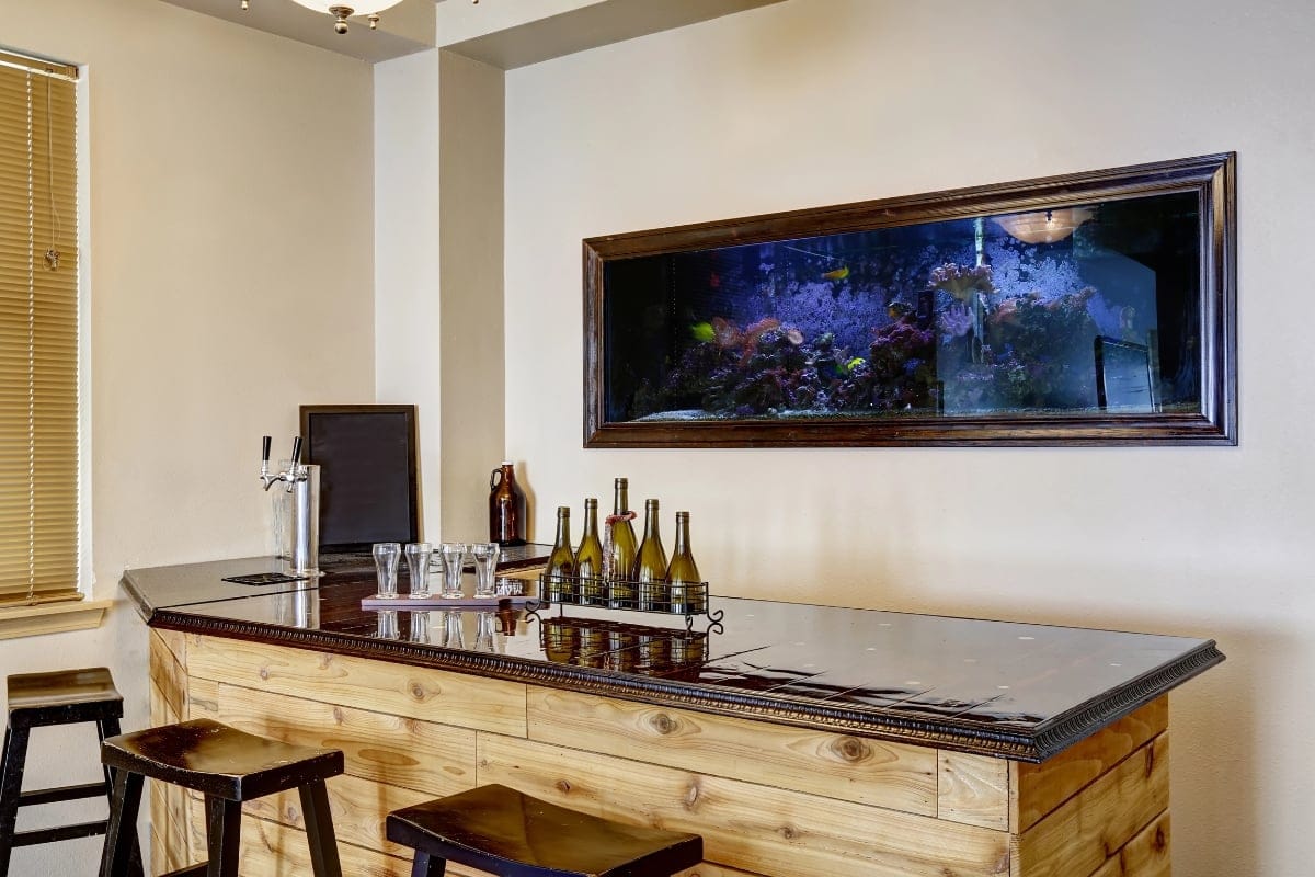 Home bar with stools, a wall-mounted fish tank, and bottles on the counter.