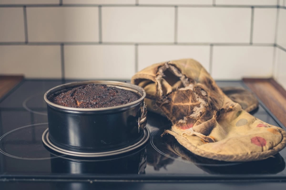 Round cake in a pan beside a worn oven mitt on a stovetop.