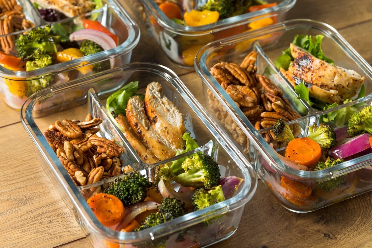 Meal prep containers with chicken, pecans, broccoli, carrots, and onions.
