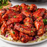 A plate of saucy chicken wings garnished with chopped parsley on shredded cabbage.