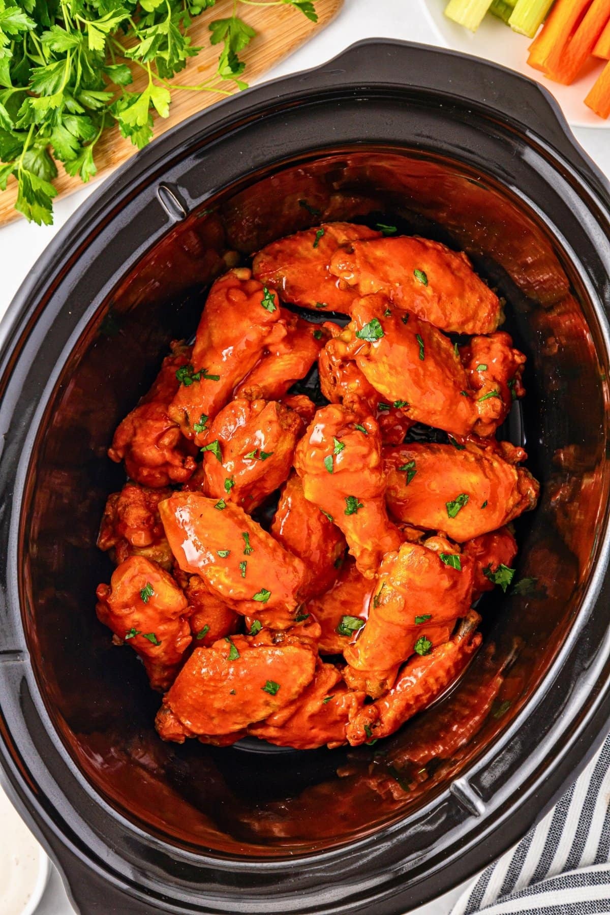 Buffalo chicken wings in a slow cooker, garnished with chopped parsley.