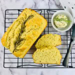 Golden rosemary bread on a cooling rack with butter and herbs on the side.
