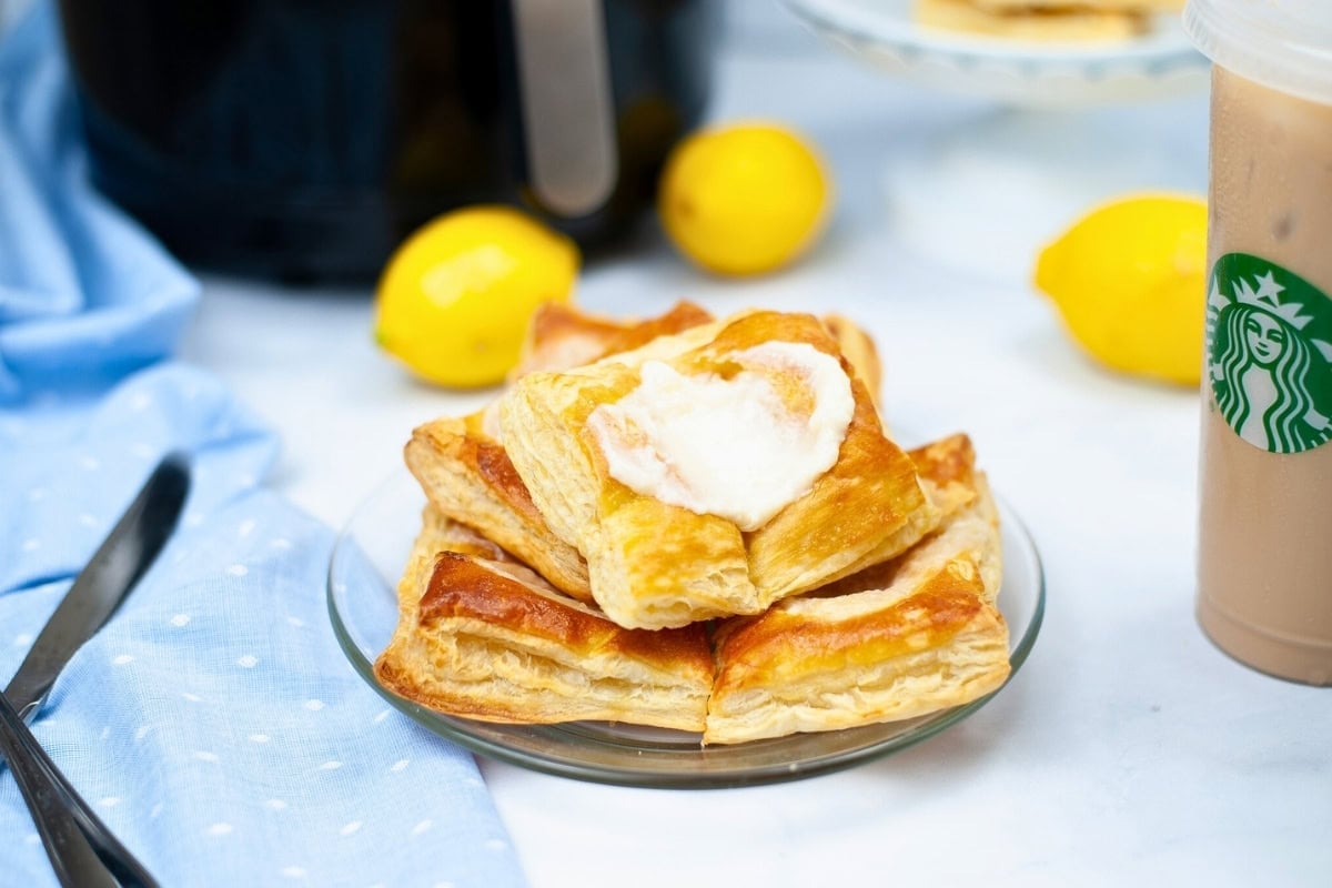 Three lemon pastries on a plate, with lemons and iced coffee in the background.