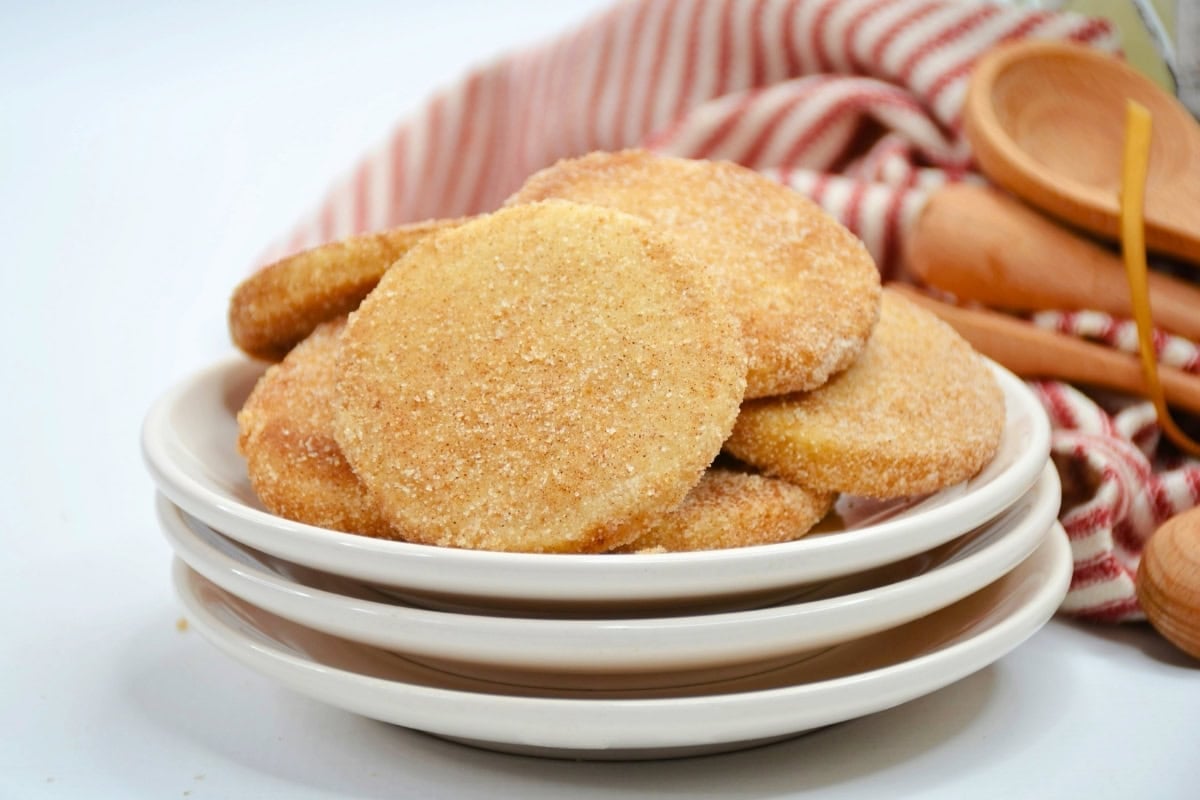 A stack of biscochitos cookies on white plates with wooden spoons and a striped cloth.