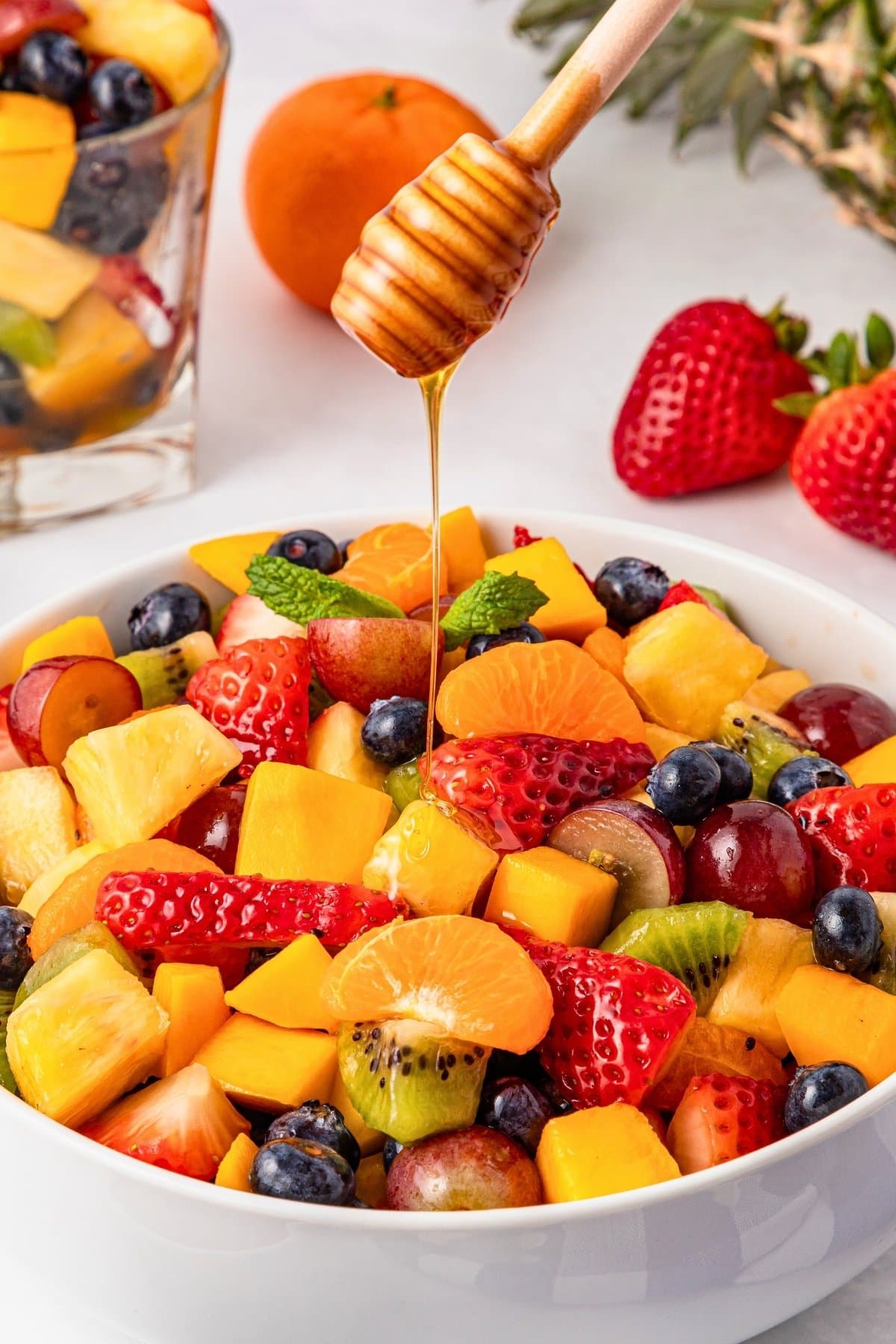 A bowl of mixed fruit salad with honey drizzled on top.