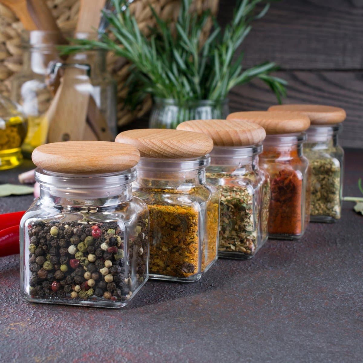 Glass jars with wooden lids filled with colorful spices on a kitchen counter.