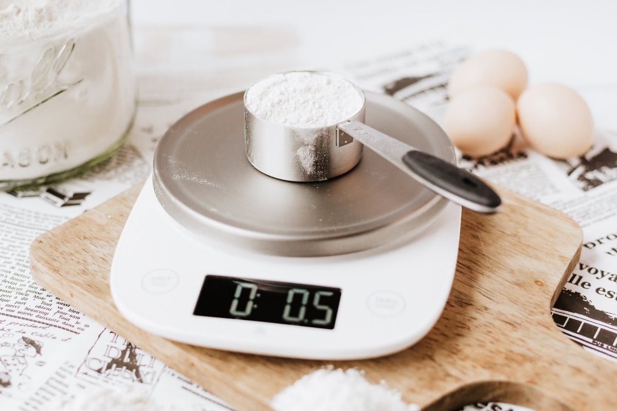 Digital scale with flour in a measuring cup and eggs nearby.