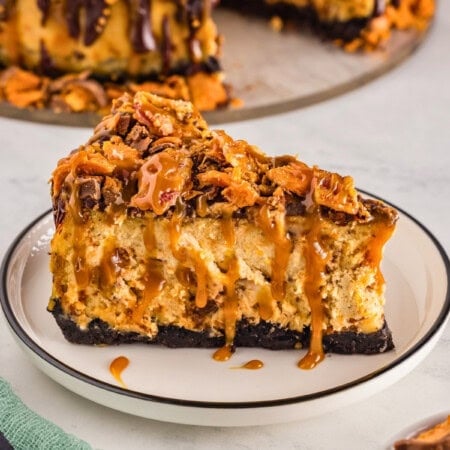 Slice of Reeses cheesecake topped with caramel and chocolate on a white plate.