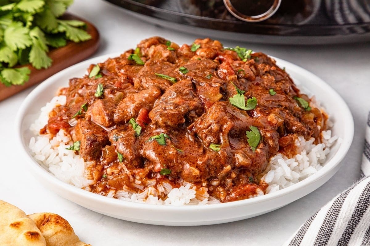 A plate of white rice topped with saucy beef curry and chopped cilantro.