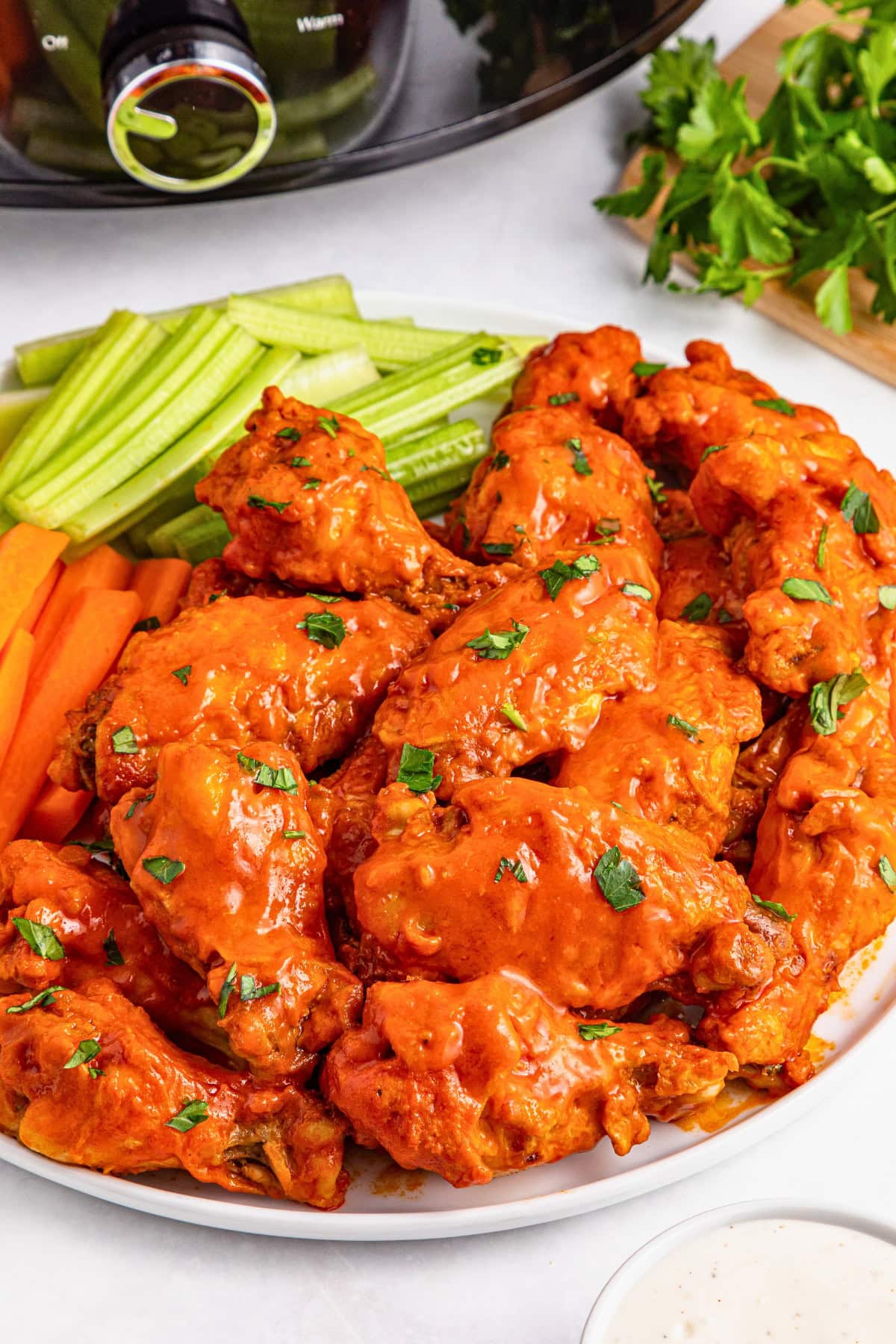 Plate of saucy buffalo chicken wings with celery, carrot sticks, and ranch dip.