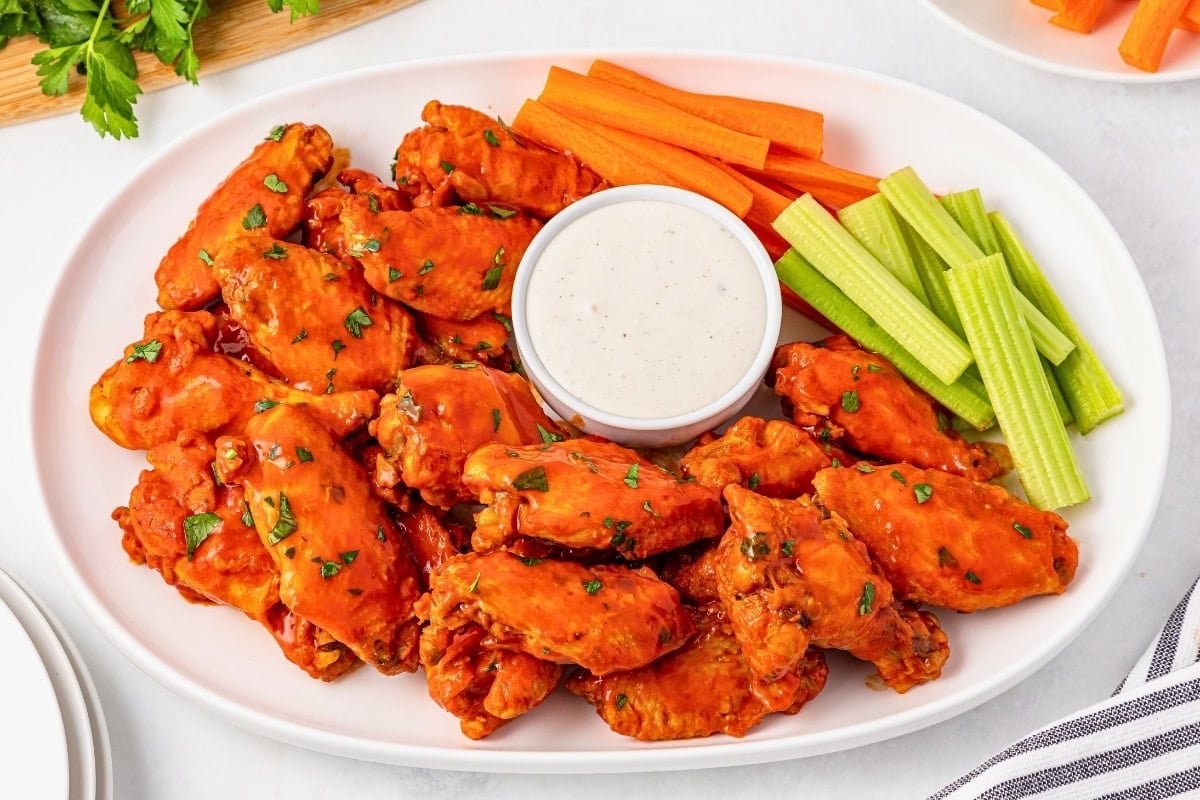 Plate of buffalo wings with ranch dip, celery, and carrot sticks.