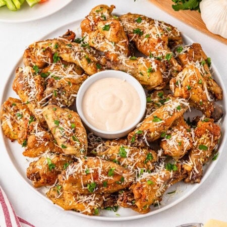 A plate of garlic parmesan wings with dipping sauce in the center.