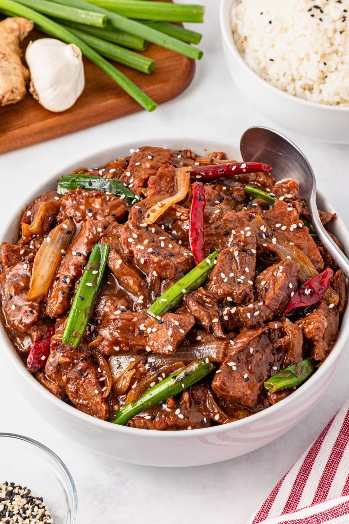 Beef with vegetables and sesame seeds in a bowl, with rice nearby.