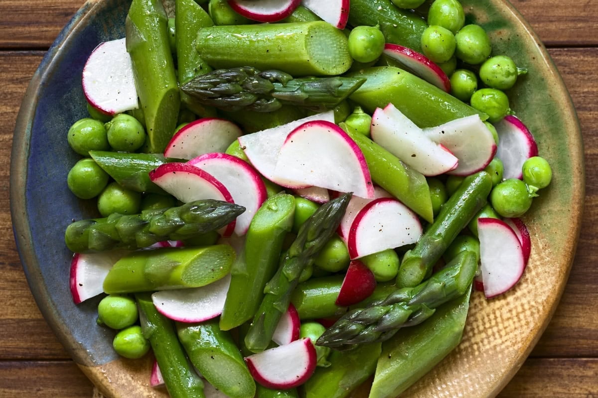 A plate of asparagus, radishes, and peas on a wooden table.