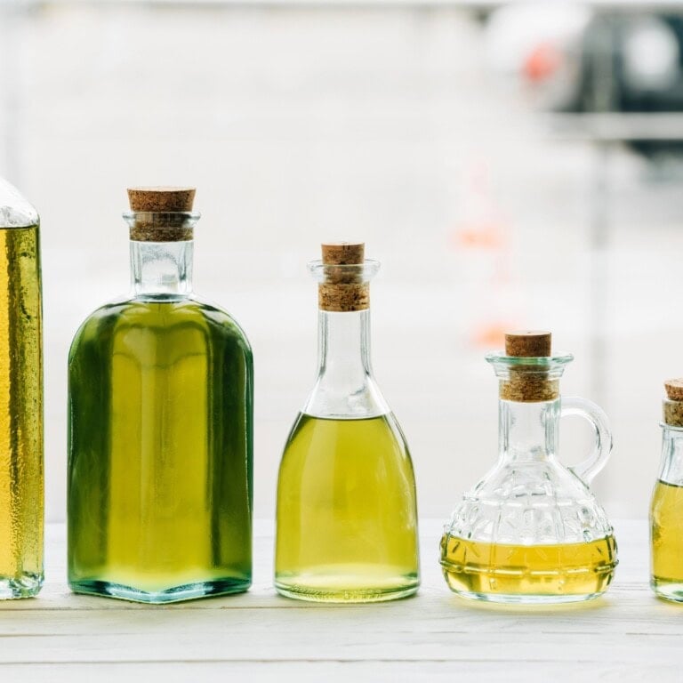 Glass bottles with corks filled with different shades of olive oil on a table.