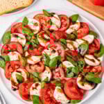 Easy Caprese Salad with tomato, mozzarella, basil, and balsamic glaze on a white plate.
