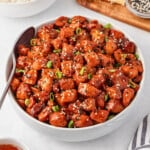 Bowl of honey garlic chicken garnished with sesame seeds and green onions.