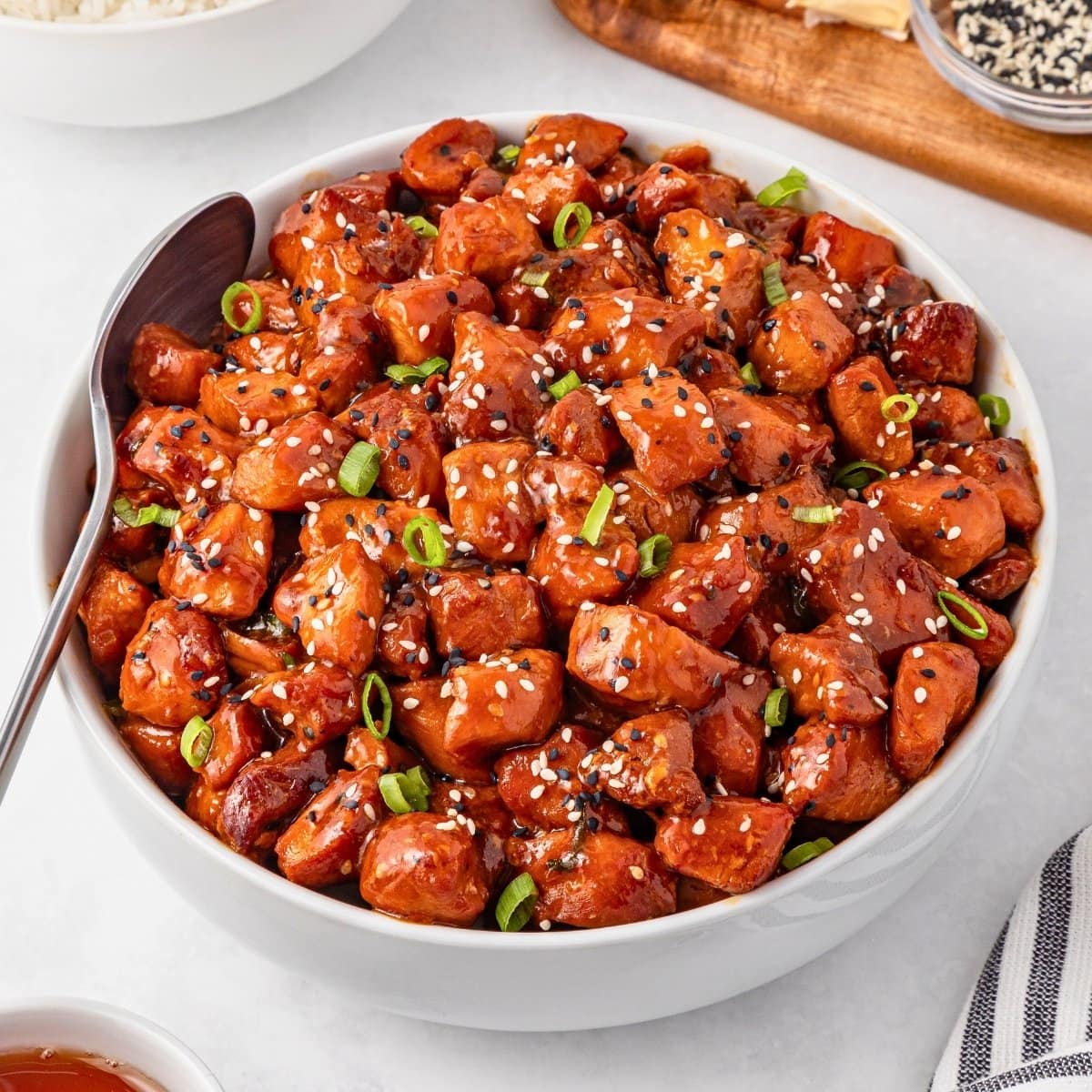 Bowl of honey garlic chicken garnished with sesame seeds and green onions.