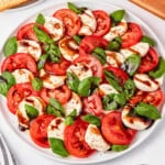 Easy Caprese Salad with tomato, mozzarella, basil, and balsamic glaze on a white plate.
