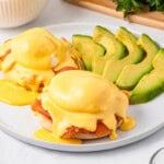 Smoked Salmon Eggs Benedict with hollandaise sauce and avocado slices on a plate.