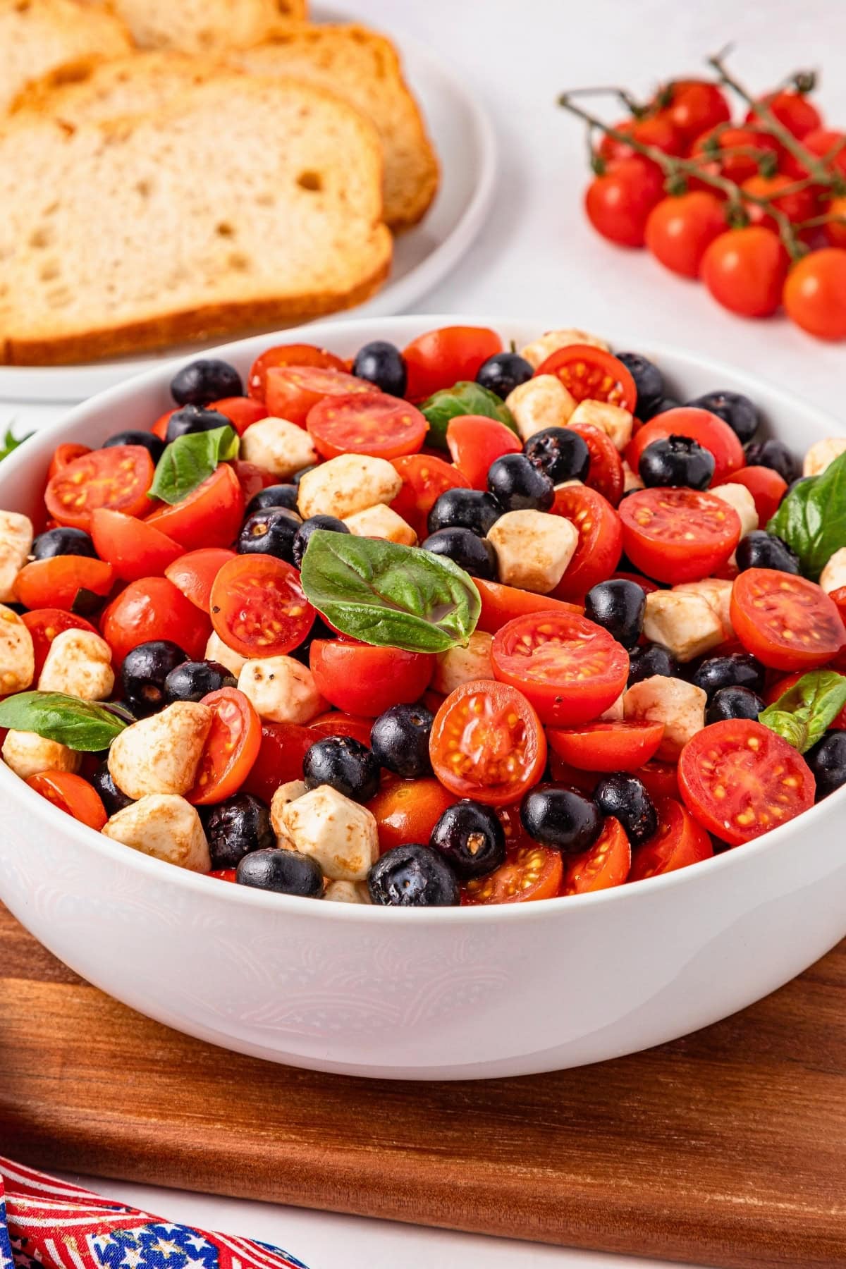A bowl of tomato, mozzarella, and olive salad with fresh basil leaves.