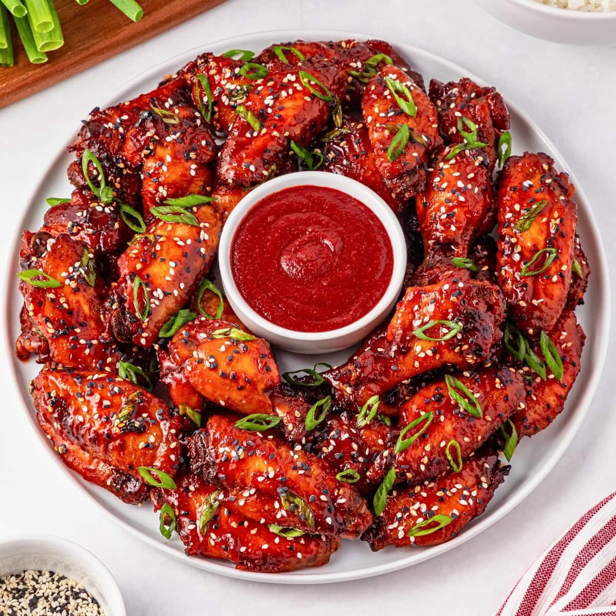 A plate of saucy chicken wings with sesame seeds, green onions, and dip.
