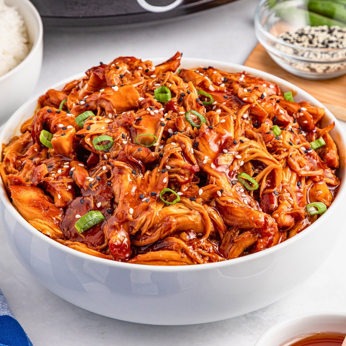 Shredded teriyaki chicken topped with green onions and sesame seeds in a white bowl.