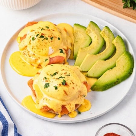 Smoked Salmon Eggs Benedict with hollandaise sauce and avocado on a white plate.